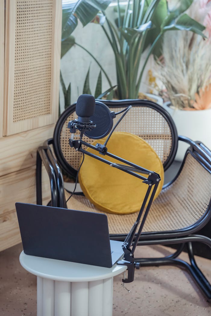 Home Modern laptop and microphone on tripod placed near wicker chair in modern studio before recording podcast